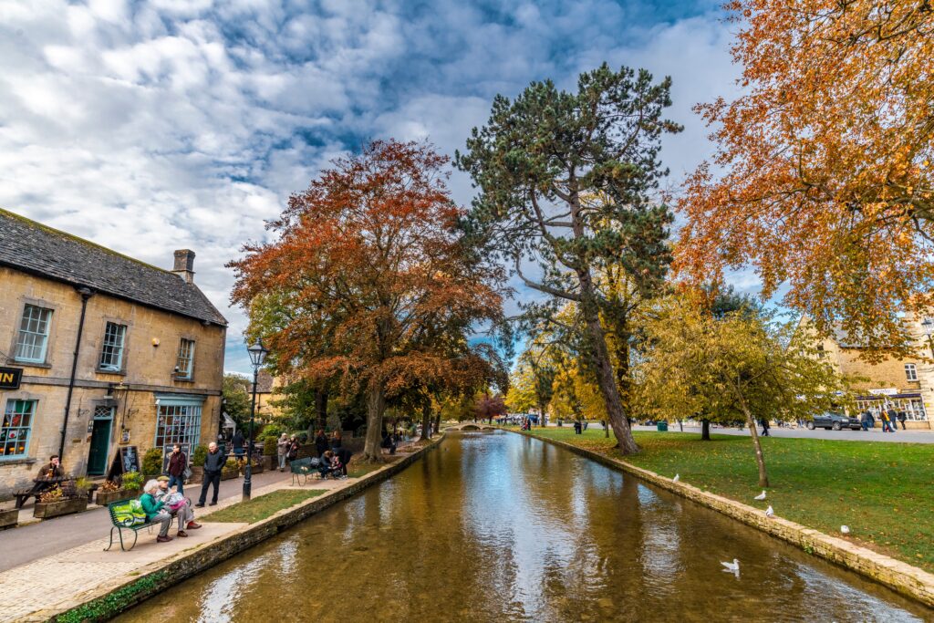 BourtonontheWater Riverside Walk Kayde Parker Bourton on the Water Riverside Walk along a scenic canal with autumn trees benches and Cotswold village buildings