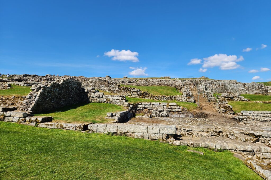 Housesteads Fort Kayde Parker Stone terraced ruins along a grassy landscape under a clear blue sky