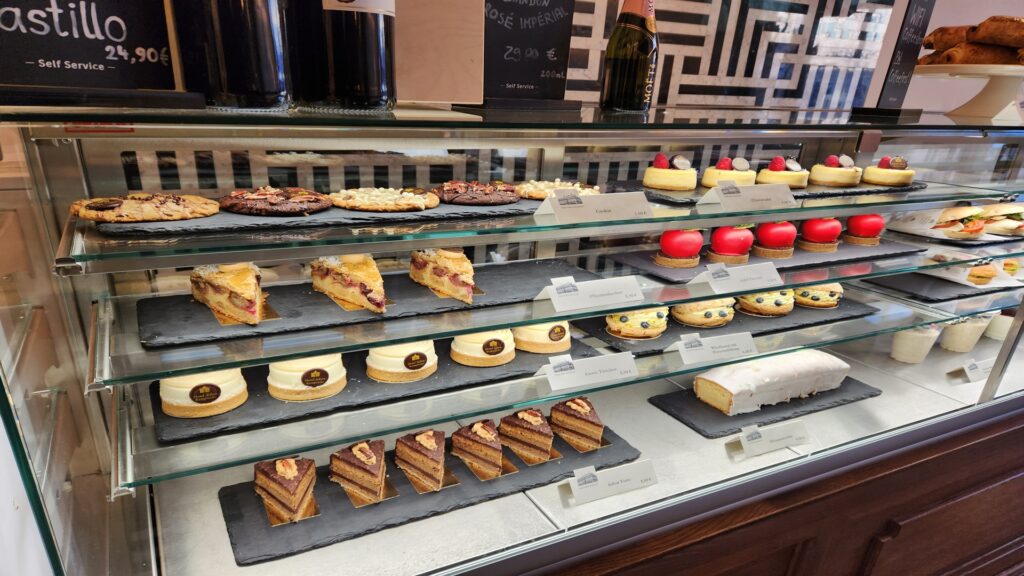 German bakery food resized Kayde Parker Assorted pastries and cakes in a glass bakery display case on black slate trays with labels in front