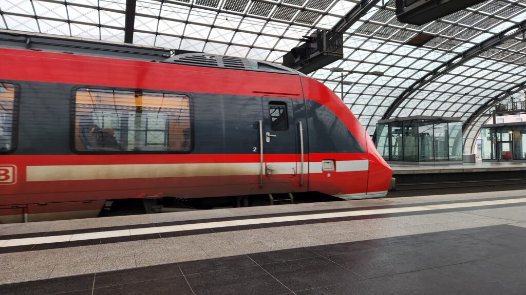 Red high speed train at a glass covered platform doors closed windows reflecting the station interior