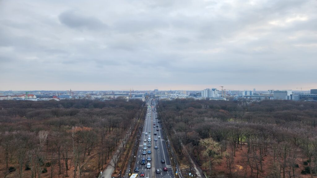 Aerial view of a multi lane road lined by leafless trees leading to a city skyline on a cloudy day